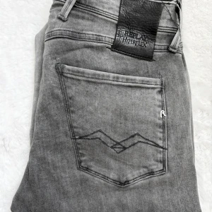 Replay Anbass Hyperflex grå jeans 29/32 - Snygga grå Replay Anbass Hyperflex jeans med klassisk femficksdesign och raka ben. Jeansen har en cool tvättad look och är tillverkade i stretchigt denim för extra komfort. Perfekta för dig som gillar stilrena och moderna jeans. Storlek W29