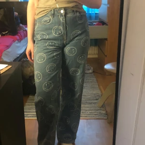 Smiley x H&M jeans med smiley-mönster - Jeans från Smiley x H&M i blå denim med vita smiley-ansikten över hela byxorna. Perfekta för dig som vill sticka ut med ett lekfullt och trendigt plagg.