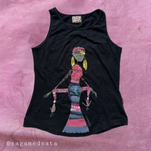 Svart linnetopp från Flamenco Stretch - Cool svart linnetopp från Flamenco Stretch med färgglad tryckt illustration av en person i lång klänning framtill. Toppen är ärmlös och har rund halsringning. Perfekt för dig som gillar unika prints och vill sticka ut lite extra.