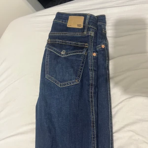 Mörkblå jeans från 157, bootcut - Snygga mörkblå jeans från 157 med klassisk femficksdesign och kontrastsömmar. Jeansenr bootcut och normal passform, perfekta till en avslappnad stil. Tillverkade i slitstarkt denimtyg med detaljerade bakfickor. Har små hål som inte alls märks och som är ihopsydd- därför så låg pris 