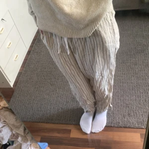 Beige randiga linnebyxor med snörning - Säljer ett par beige linnebyxor med tunna svarta ränder. Byxorna har avslappnad passform, resår i midjan och snörning framtill. Perfekta för varma dagar och chill vibes. Lätta och luftiga med raka ben.