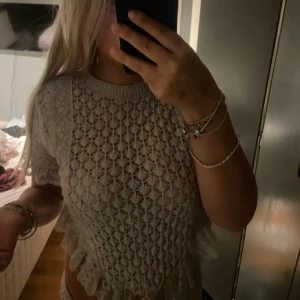 Vit spetsig blus med volang - Supersöt vit blus med spetsmönster och volangdetaljer längs nederkanten. Kortärmad och croppad modell som ger en trendig vibe. Perfekt att styla med jeans eller kjol för en fräsch look.