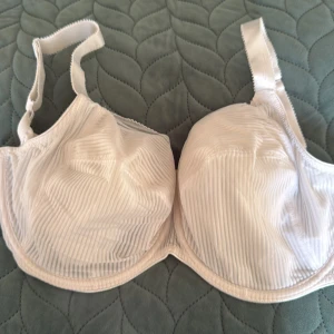 Vit randig bh med breda axelband - Säljer en vit bh från Fantasie  med diskret randigt mönster och breda, justerbara axelband. Bh:n har bygel och hakknäppning bak. Materialet känns mjukt och följsamt, perfekt för dig som vill ha både stöd och stil. Passar dig som gillar klassisk och enkel design.