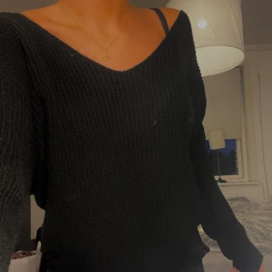 Svart stickad tröja med öppen rygg - Svart stickad tröja med v-ringning både fram och bak, vilket ger en snygg öppen rygg. Tröjan har lång ärm och en loose passform som känns chill och trendig. Perfekt att styla med jeans eller kjol för en avslappnad look.