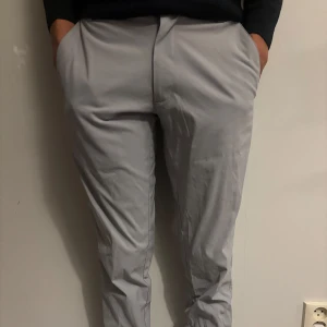 Golf byxor  - Snygga ljusgrå chinos från FootJoy med klassisk passform och raka ben. Byxorna har bälteshällor, sidofickor och två bakfickor med diskret logga. Tillverkade i mjukt och lätt bomullsmaterial med lite stretch för extra komfort.