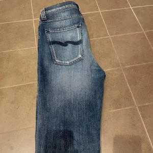 Nudie jeans - Säljer ett par klassiska blå jeans från Nudie Jeans i modellen 28/32. Jeansen är i slimmad modell, fem fickor och dragkedja. Snygg tvätt med lätt slitning och Nudie-logga på bakfickan. Bra skick. 