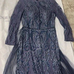 Mörkblå glittrig långklänning Jolie Bride - Säljer en magisk mörkblå långklänning från Jolie Bride med glittriga paljettdetaljer och transparenta långärmar. Klänningen har ett elegant mönster och är tillverkad i ett skimrande syntetmaterial med tyll. Perfekt för bal eller festliga tillfällen!