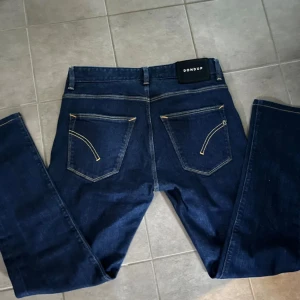 Dondup Jeans - Snygga mörkblå jeans från Dondup med klassisk femficksdesign och kontrastsömmar. Jeansen har raka ben och normal passform, tillverkade i mjukt denimtyg. Bakfickorna har unika broderade detaljer och märkespatch i midjan. Storleks taggarna på insidan har blivit av klippta men funkar mycket bra ändå!