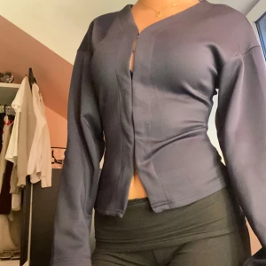 Mörkblå figursydd topp - Säljer en mörkblå, figursydd topp med v-ringning och långa ärmar. Koftan har en clean look utan synliga knappar och är tillverkad i ett mjukt, stretchigt material som sitter snyggt på kroppen.