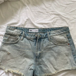 Ljusblå jeansshorts från Zara - Snygga ljusblå jeansshorts från Zara med fransig kant och klassisk femficksdesign. Shortsen har normal passform, bälteshällor och slitna detaljer. Aldrig använda eftersom jag köpte fel storlek.🥰