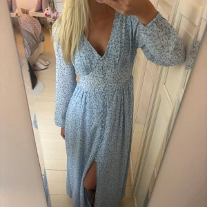 Ljusblå långklänning med blommigt mönster - Säljer en ljusblå adoore liknande långklänning med små blommor, v-ringad och med lång ärm. Använd 1 gång