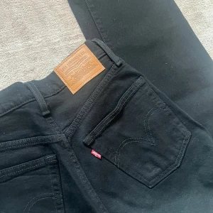 Svarta Levi's 501 jeans straight fit - Svarta Levi's 501 jeans med klassisk straight fit och hög midja. Jeansen har fem fickor, silverfärgad knapp och nitar samt den ikoniska bruna läderpatchen bak. Tillverkade i kraftig bomull med snygg svart tvätt och röda Levi's-taggen på bakfickan mycket bra skick.
