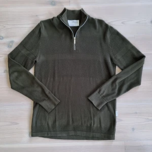 Olivgrön stickad tröja Selected Homme - Säljer en olivgrön stickad tröja från Selected Homme i storlek M. Tröjan har en halv dragkedja vid halsen, ribbade muddar och ett diskret strukturerat mönster över bröstet och ärmarna. Perfekt för lager-på-lager under hösten och vintern.