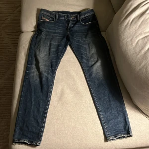 Blå jeans från Diesel - Säljer ett par klassiska blå jeans från Diesel Industry med snygga slitningar och kontrastsömmar. Jeansen har raka ben, fem fickor och detaljer med Diesel-logga på bakficka och myntficka. Perfekta till sneakers och hoodie för en avslappnad look. Använda endast 4 gånger så i princip nyskick. Nypris är ca 2200kr!