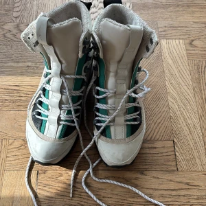 Diesel höga sneakers i vitt och grönt - Unika höga sneakers från Diesel i vitt, grönt och svart med coola detaljer. Skorna har snörning, grov sula och vadderad insida för extra komfort. Materialmix av skinn och syntet, med svarta detaljer och Diesel-logga baktill. Perfekta för dig som vill sticka ut.