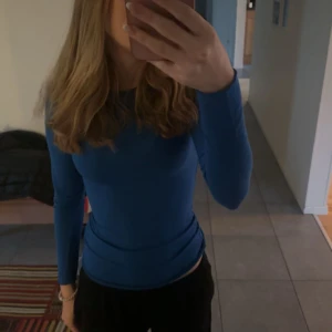 Blå långärmad topp - Säljer en enkel och stilren blå långärmad topp med tight passform. Perfekt att matcha med jeans eller kjol för en clean look. Tunn och stretchig i materialet, vilket gör den riktigt bekväm att bära.