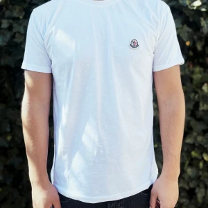Vit Moncler t-shirt med logga - Fräsch vit t-shirt från Moncler med rund hals och korta ärmar. Diskret Moncler-logga broderad på bröstet. T-shirten är i mjuk bomull och har en clean, klassisk passform som funkar till jeans eller shorts.                          Nypris: 2000kr GORILLAPRIZE:1120kr            Skick:10/10 oöppnad         KVITTO MEDKOMMER     