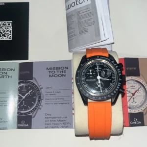 Omega x Swatch MoonSwatch Speedmaster - Säljer en Omega x Swatch MoonSwatch Speedmaster Mission to the Moonphase med svart urtavla, vita detaljer och orange gummiband. Klockan har kronograf, tachymeter och levereras med originalförpackning, extra svart textilband och box. Grym design för dig som gillar statement-accessoarer.ny pris 6999kr men jag säljer för 3449kr det ingår även båda boxarna man ser 
