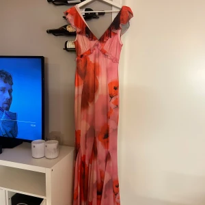 Rosa långklänning med volang från Bubbleroom - Supersnygg långklänning i rosa och rött med blommigt mönster, djup v-ringning och volangdetaljer vid axlar och byst. Klänningen har figurnära passform och är ärmlös, perfekt för sommarkvällar och fester 🩷 Använd 1 gång, älskade klänningen men den var tyvärr för lång för att jag ska kunna använda den 🩷 nypris 899, nu nedatt till 699kr. Men kommer sälja för 550kr🩷