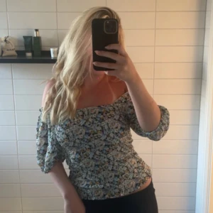 Blommig offshoulder blus från Vila - Supersöt blommig blus från Vila med offshoulder och trekvartsärmar. Toppen har smockad passform som sitter snyggt och ger en feminin siluett. Färgerna går i blått, vitt, gult och svart på ett ljust tyg💞💞💞Aldrig använd! Helt ny med prislapp 