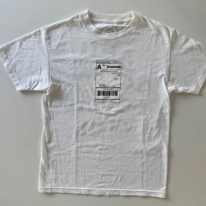 Vit Anti Social Social Club t-shirt - Vit t-shirt från Anti Social Social Club i storlek M med tryck av en fejkad fraktsedel på bröstet och stor svart logga på ryggen. Klassisk rund hals och korta ärmar. Perfekt för dig som gillar streetwear och statement-plagg.