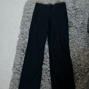 Svarta kostymbyxor från Stockh LM - Snygga svarta kostymbyxor från Stockh LM med raka ben och klassisk passform. Byxorna har hällor för bälte, två bakfickor och en liten metallring bak. Perfekta för en clean och stilren look. Luftiga men ullmix så de håller värmen!