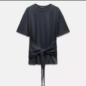 Svart t-shirt med knyt i midjan - Cool svart t-shirt från Zara med korta ärmar och rund hals. Den har en unik knyt-detalj i midjan som ger en snygg siluett. Materialet känns mjukt och skönt, perfekt för dig som gillar stilrena plagg med en twist.