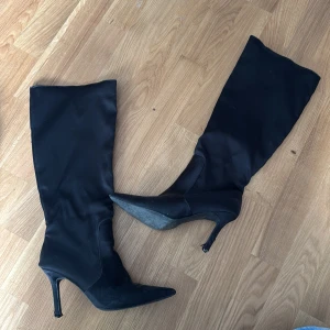 Svarta höga stövlar med klack - Svarta höga stövlar med spetsig tå och smal hög klack. Står att det är stl 5 vilket motsvarar 38 men skulle säga att det är mer 39/40