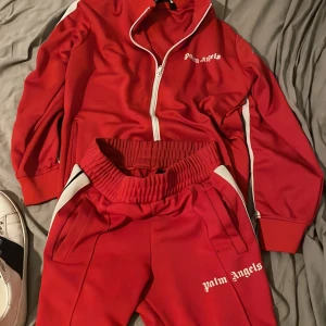 Säljer ett rött Palm angels sätt byxor xs tröja M - Går att köpa separat oxå om man har några frågor så är de vara arg skriva.!Riktigt snygga röda mjukisbyxor från Palm Angels med vit logga på benet och vita ränder längs sidorna. Byxorna har bred resår i midjan och är gjorda i ett glansigt polyestermaterial som ger en sportig vibe. Perfekta för dig som gillar streetwear.