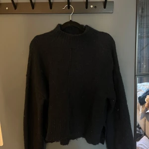 Marinblå stickad tröja med hög krage - Mysig marinblå stickad tröja med hög ribbad krage och lång ärm. Tröjan har en lite loose passform och rå kant nertill för en avslappnad vibe. Perfekt att slänga på sig när det är kallt ute.