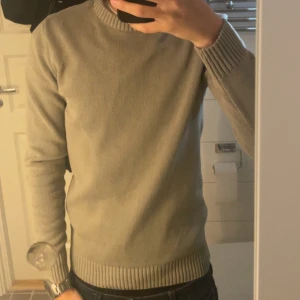 Grön stickad tröja - Säljer en enkel och stilren grön stickad tröja med rund hals och ribbade muddar vid ärmslut och nederkant. 