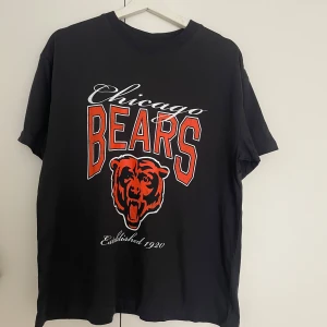Chicago Bears t-shirt från H&M - Svart t-shirt från H&M med Chicago Bears tryck i rött och vitt samt en stor björnlogga framtill. Rund hals och korta ärmar. Materialet är mjuk bomull med 3% syntet. Perfekt för dig som gillar amerikansk fotboll och sportig streetstyle.