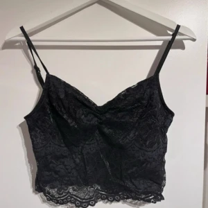 Spetsig topp  - Svart topp i spets med tunna axelband och v-ringning. Är inte helt säker på vart toppen är ifrån