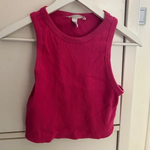 Rosa ribbad linnetopp från H&M - Snygg rosa croppad linnetopp från H&M med ribbad struktur. Modellen är ärmlös med breda axelband och rund halsringning. Perfekt för varma dagar eller lager på lager-stil.