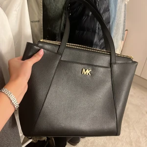 Svart Michael Kors axelväska i skinn - Snygg svart axelväska från Michael Kors i stilrent skinn med guldfärgade detaljer och MK-logo framtill. Köpt i sthlm för x antal år sedan på Micael kors butiken. 