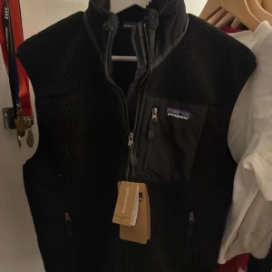 Svart fleeceväst från Patagonia - Säljer en svart Patagonia väst med svarta fickor och dragkedjor. Är i storlek S men passar åt det större hållet. Helt ny med prislapp kvar! Hör av er vid funderingar.