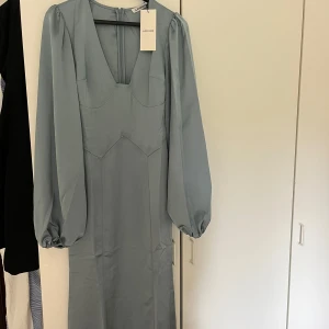 Ljusblå långklänning från Adoore - Superfin ljusblå långklänning från Adoore med v-ringning och långa puffärmar. Klänningen har markerad midja och dragkedja bak. Materialet är mjukt och har en lätt glansig finish som ger en lyxig känsla. Klänningen är aldrig använd och prislappen finns kvar🫶🩵