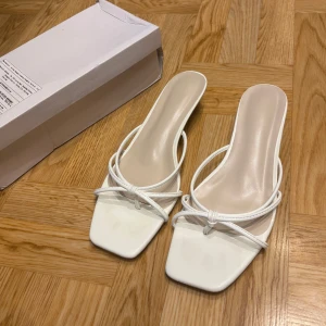 Låga klackarskor/sandaler - Snygga vita sandaler med smala remmar, de har en fyrkantig tå och låg klack som ger en stilren vibe. Perfekta för dig som gillar minimalistisk design och vill ha något som sticker ut. Endast använda vid 1 tillfälle, säljer pga dom var lite för stora för mig. Är lite slitna, syns på dom 2 sista bilderna.