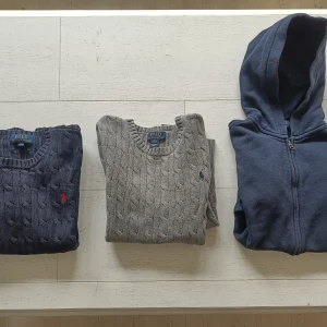 3 st Tröjor Polo Ralph Lauren - Säljer en mörkblå kabelstickad tröja från Polo Ralph Lauren med röd broderad logga på bröstet. Tröjan har rund halsringning och långa ärmar, perfekt för lager-på-lager under höst och vinter. Polo Ralph Lauren tröjor   storlek 140-150 cl / M kids /10-12 year  Kabelstickad marinblå tröja  Pris 5000 kr (Nypris 1495 kr) Kabelstickad grå tröja  Pris 500 kr (Nypris 1495 kr) Marinblå hoodie  Pris 250 kr (Nypris 1195 kr)  Paketpris alla 3 för 1000 kr  