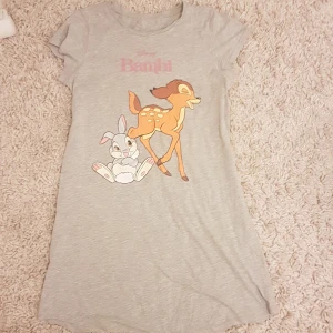 Grå Disney Bambi kortklänning - Supersöt grå kortklänning med tryck av Bambi och Stampe framtill. Mjuk bomullskänsla, rund hals och korta ärmar. Perfekt för dig som älskar Disney och vill ha en chill och lekfull stil. PRIS KAN DISKUTERAS!