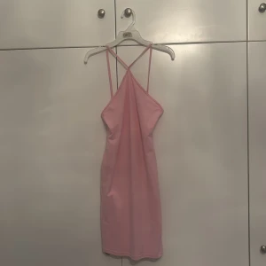 Rosa  klänning med smala axelband - Supersöt rosa kort klänning med smala korsade axelband och enkel design. Klänningen har en figurnära passform och är perfekt för varma dagar. Tillverkad i mjukt material som känns skönt mot huden. Enkel men ändå riktigt snygg och lätt att styla.
