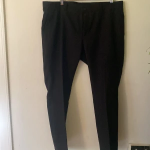 Svarta kostymbyxor med tapered fit - Snygga svarta kostymbyxor med avsmalnande ben och klassisk design. Byxorna har bälteshällor, knapp och dragkedja framtill samt två bakfickor. Perfekta för en clean och stilren look. Materialet är slätt och känns bekvämt mot huden.      Srl- W38/L30