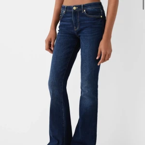Mörkblå bootcut jeans - Snygga mörkblå jeans med bootcut passform och klassiska gula sömmar. Jeansen har fem fickor och stängs med knapp och dragkedja. Perfekta för en trendig och avslappnad look.