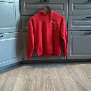 Röd hoodie från Gina Tricot med tryck - Röd hoodie från Gina Tricot med vit text 'MA CHÉRIE' och en stjärna på bröstet. Tröjan har huva med snörning och är tillverkad i mjuk bomullsmix. Perfekt för dig som gillar en chill och snygg stil.