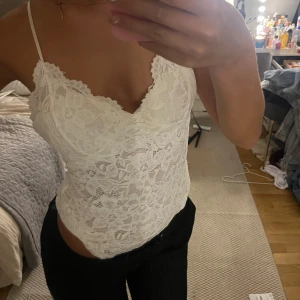 Vit spetsig linnetopp med smala band - Supersöt vit linnetopp med tunna axelband och v-ringning. Hela toppen är täckt av blommig spets som ger en romantisk och trendig vibe. Perfekt att styla med jeans eller kjol för en fräsch look. Sitter tajt och framhäver figuren på ett snyggt sätt.