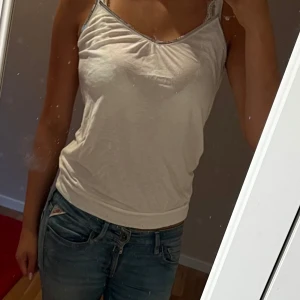 Vit paljettkantad linnetopp Express XS - Säljer en vit linnetopp från Express i storlek XS. Toppen har smala axelband och en snygg v-ringning med silvriga paljetter längs kanten. Materialet är mjukt och lätt, perfekt för varma dagar. Enkel men ändå glittrig detalj som gör den extra fin.