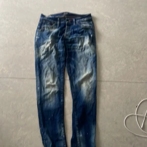 Blå jeans från Jack & Jones - Säljer ett par blå jeans från Jack & Jones med coolt sliten och tvättad look. Jeansen har klassisk femficksdesign, kontrastsömmar och detaljer i vitt och grått. Materialet är jeans och passformen är rak med normal midja.