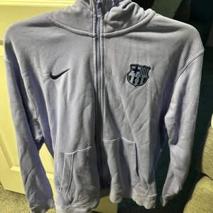 Ljuslila Nike FC Barcelona hoodie - Säljer en ljuslila FC Barcelona zip hoodie. Tröjan är i bra skick (8/10) och är i storlek L. 