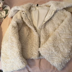 Beige teddyjacka med dragkedja - Supermysig teddyjacka i beige med fluffig och krullig yta. Jackan har dragkedja framtill och en avslappnad passform. Perfekt för kalla dagar när du vill vara både varm och snygg. Fodrad insida för extra komfort.