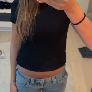 Svart ribbad croppad topp - En svart, ribbad topp/ t-shirt med korta ärmar. Toppen har en basic och stilren design. De står ingen storlek men jag brukar ha XS/S i kläder. 